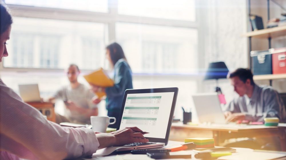 Team work process. Young business crew in big loft office. Laptop with graph, analysing marketing. Film effect, blurry background, lens flare effect
